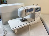 Machine on table with extension table attached, hard cover behind and foot pedal cable visible