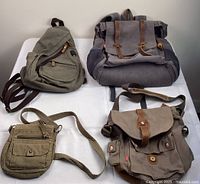 Four canvas bags in neutral tones displayed on a flat surface showing overall sizes and styles