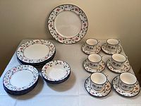 Overview of entire ceramic dish set showing plates, bowls, teacups, and saucers with floral pattern.