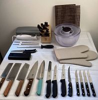 Photo showing the entire assortment of kitchen knives, tools, salad spinner, and oven mitts arranged on a white surface.