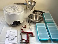 Photo showing the assembled Cosori 5 tray food dehydrator, the stainless steel funnel and bowl, red metal apple peeler, manual, strainer, and scissors on display.