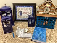 Overview of three Doctor Who TARDIS decor items, framed cross-stitch sign, wind-up clock toy, dice, and a book/notebook