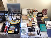 Overview photo showing the assembled lot including Dymo Rhino 4200 label printer, notebooks, pens, crafting tapes, display stands, and storage trays.