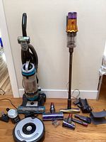 Overview of Dyson stick vacuum, Bissell upright, Roomba and assorted attachments on floor