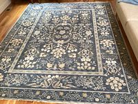 Full view of navy rug with beige floral pattern on hardwood floor