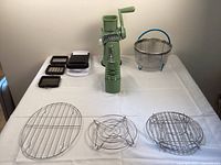 Overview of all items showing green manual rotary chopper, metal racks, and mesh basket arranged on table