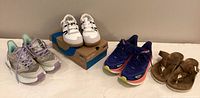 Four pairs of women's shoes displayed including beige/lavender Hoka, white Zero shoes, blue Hoka shoes, and brown Birkenstocks facing forward.