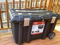 Closed view of the Husky black mobile job box showing its sturdy design, metal latches, keyed lock, and attached wheels.