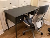 Side angle showing the dark grey desk with two drawers and the office chair pushed under it.