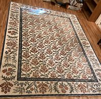 Full view of rectangular cream area rug on hardwood floor showing floral pattern and border