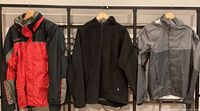 Three jackets hanging side by side on rack: Columbia large red/black, black fleece, gray REI rain jacket