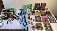 Wide shot showing all Minecraft items including inflatable swords, figurines, books, and games spread on table.