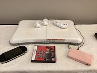 Wii Balance Board, two white nunchuck controllers, one white Wii remote with wrist strap, pink Nintendo DS handheld, and Nintendo DS game with Japanese cover art.