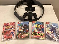Games and Ring Fit accessory spread out on a surface showing all four game cases and the black Ring Fit controller device with leg strap.