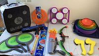 Photo showing entire lot of outdoor toys including Koosh pickleball paddles, Nerf Rival blaster, colorful stacking cones, kids bow with arrows, foam axes and Rubber Band Shooter kit.