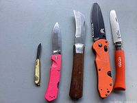 Top view of five knives laid flat showing handles and blades, including pink folding knife, wooden-handled knife, orange Benchmade, small cream knife, and Opinel Inox.