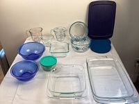 Full view of all items including blue glass bowls, measuring cups, glass baking dishes with lids, and storage bowls with lids arranged on a table.