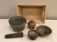 View showing the mortar, pestle, ceramic jar with stopper, two bowls, and wooden box on a white surface.