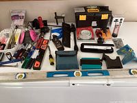 Various tools arranged on a white surface including hand tools, levels, caulking guns, respirator mask, tool box, and masking tape.