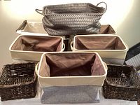 Overview photo showing all four 2-toned canvas totes with brown liners, three small brown baskets, and one large black woven tote stacked on top.
