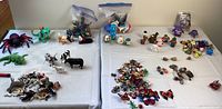 Wide view of toy collection spread on a white sheet showing multiple groups of bugs, farm animals, Pokémon, and insect figurines.