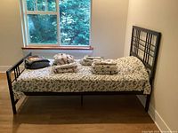 Black metal twin bed frame fully assembled with six sets of twin sheets arranged on the mattress area in front of a window.