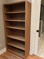 Full front view of wooden bookshelf showing five shelves and natural wood grain finish
