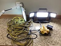 LED work light turned on, showing brightness and three panels, next to yellow extension cord and white desk lamp.