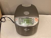 Front view of stainless steel rice cooker with digital control panel and power cord.