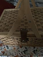 Close-up photo of the wicker picnic basket showing light tan woven material, wooden handles, and brown leather latch with brass button.
