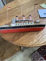 Side view of metal ship model on table showing hull colors, windows, masts with flags, and smokestacks
