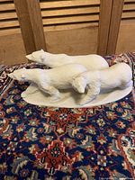 Side angle showing the full trio of polar bears on base, placed on patterned carpet with wooden background.