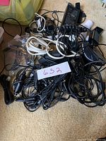 Photo showing tangle of various black and white charging cables, connectors, and telephone cords spread on beige carpet.