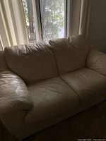 Photo of cream colored Italian leather love seat from front and left side showing armrest, cushions and overall condition.