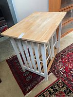 Photo showing oak top rectangular wooden table with white painted slatted base and storage shelf, placed on a patterned rug indoors.