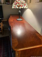 Profile view of large dark wood dresser showing top surface, minor scratches, decorative carving on corner, and drawer handles.