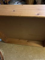 Top-down view of rectangular wooden under bed storage box showing the wooden surface and rectangular frame with knots in the wood.