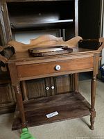 Front view of the vintage wooden table showing a single drawer with a white knob, decorative back panel, turned legs, and lower shelf.