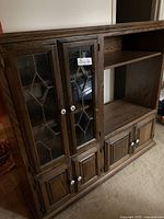 Front view of dark wood cabinet with leaded glass upper doors and lower wood doors, white knobs visible