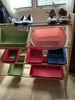 Storage rack with metal frame and multiple colored plastic bins, placed near window and carpet.