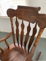 Close-up of top portion showing carved wood, spindle back supports, medium brown wood finish.