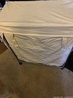 Photo showing folded beige cotton cover with pockets draped over metal frame of linen cart.