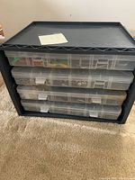 Rack holds 4 clear plastic hardware organizers containing assorted screws, nails, and fasteners; lid visible on top container