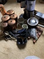 Photo showing copper pots with lids, electric coffee maker, ceramic mugs, black cooking utensils and more