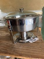 Front view of the large stainless steel chafing dish with glass lid, showing the metal frame stand and dual side handles.