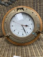 Close-up image of the nautical clock showing brass casing, wooden base, and clock face
