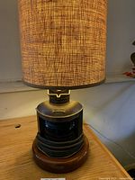 Photo showing burlap shade glowing on wooden and metal nautical lamp base from front angle.