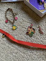 Photo of Disney charm bracelet with Flounder and other charms, two enamel pins featuring Mickey and Minnie Mouse, and a red strap with Mickey's head.