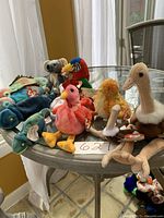 Photo showing 8 Beanie Babies and 3 Teenie Beanie Babies on a round glass table. Animals include birds, a koala, a hippo, and an ostrich named Iggy, all with Ty heart-shaped tags.