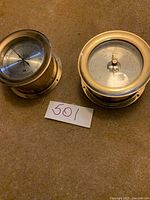 Pair of brass nautical instruments showing hygrometer and temperature gauge faces and cases.